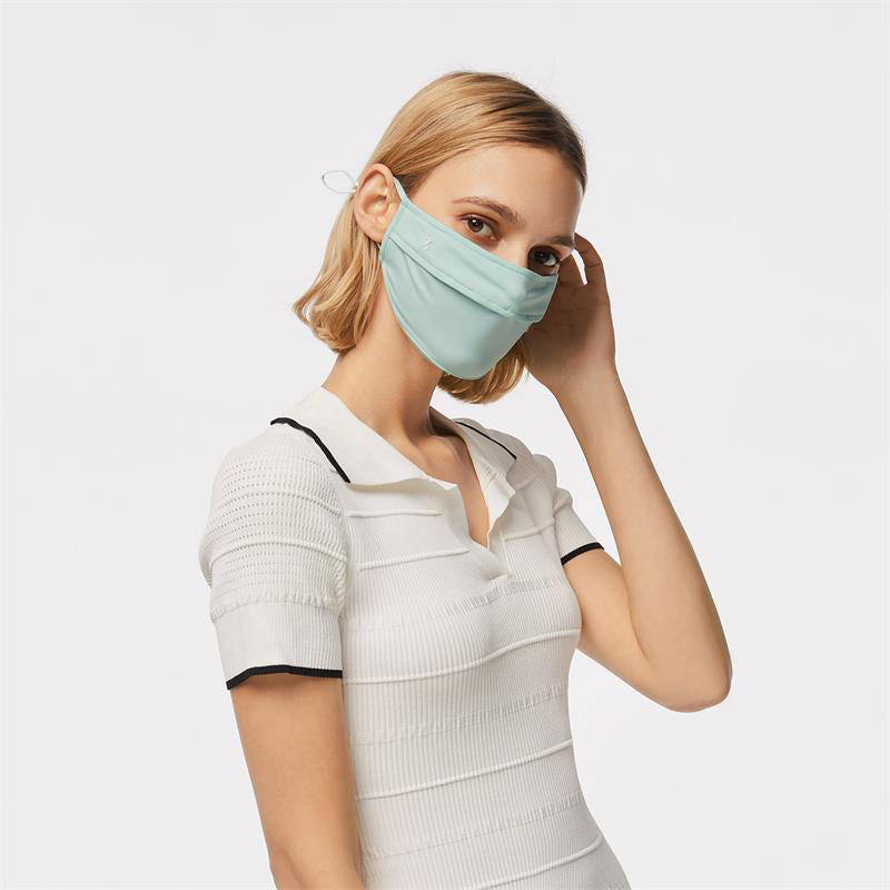Blonde woman wearing a light mint-green UPF50+ face mask layered with a white top — the foundation piece for a sun-mask stack.