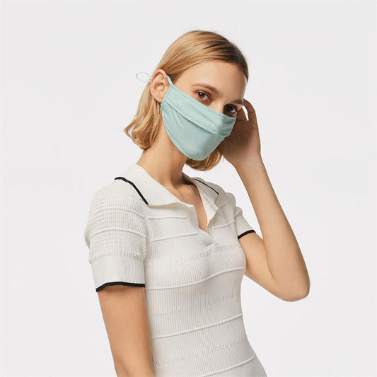 Blonde woman wearing a light mint-green UPF50+ face mask layered with a white top — the foundation piece for a sun-mask stack.