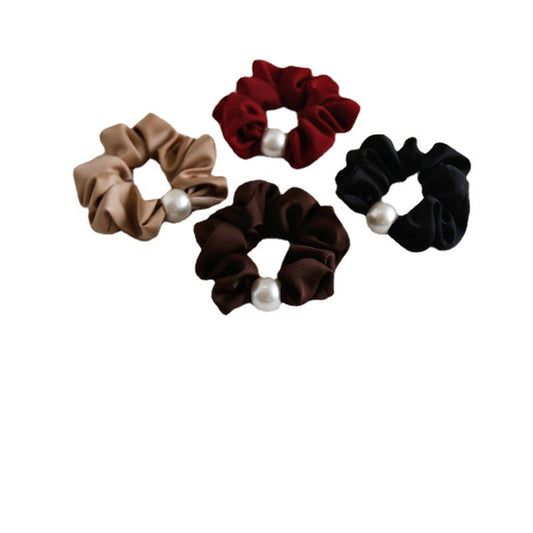 Four satin scrunchies in beige, red, brown, and black, each adorned with a single white pearl-like bead, arranged on a plain white background.