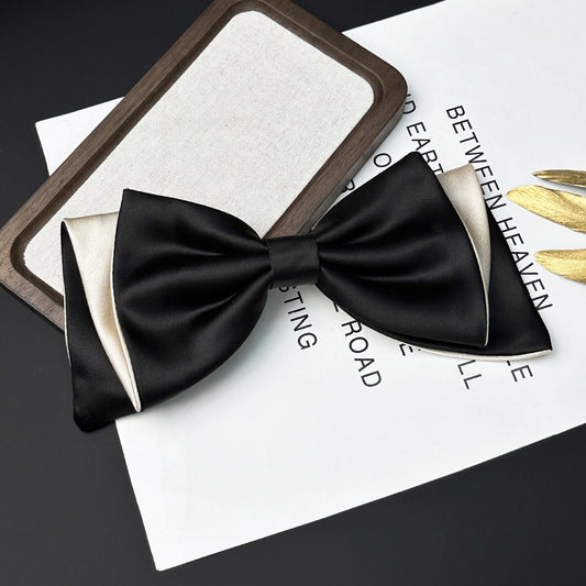 Black satin bow tie with cream-colored inner lining resting on a white paper with printed text next to a wooden-framed rectangular object