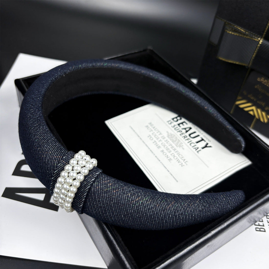 Navy blue denim-textured headband with triple-row pearl embellishment on a black box