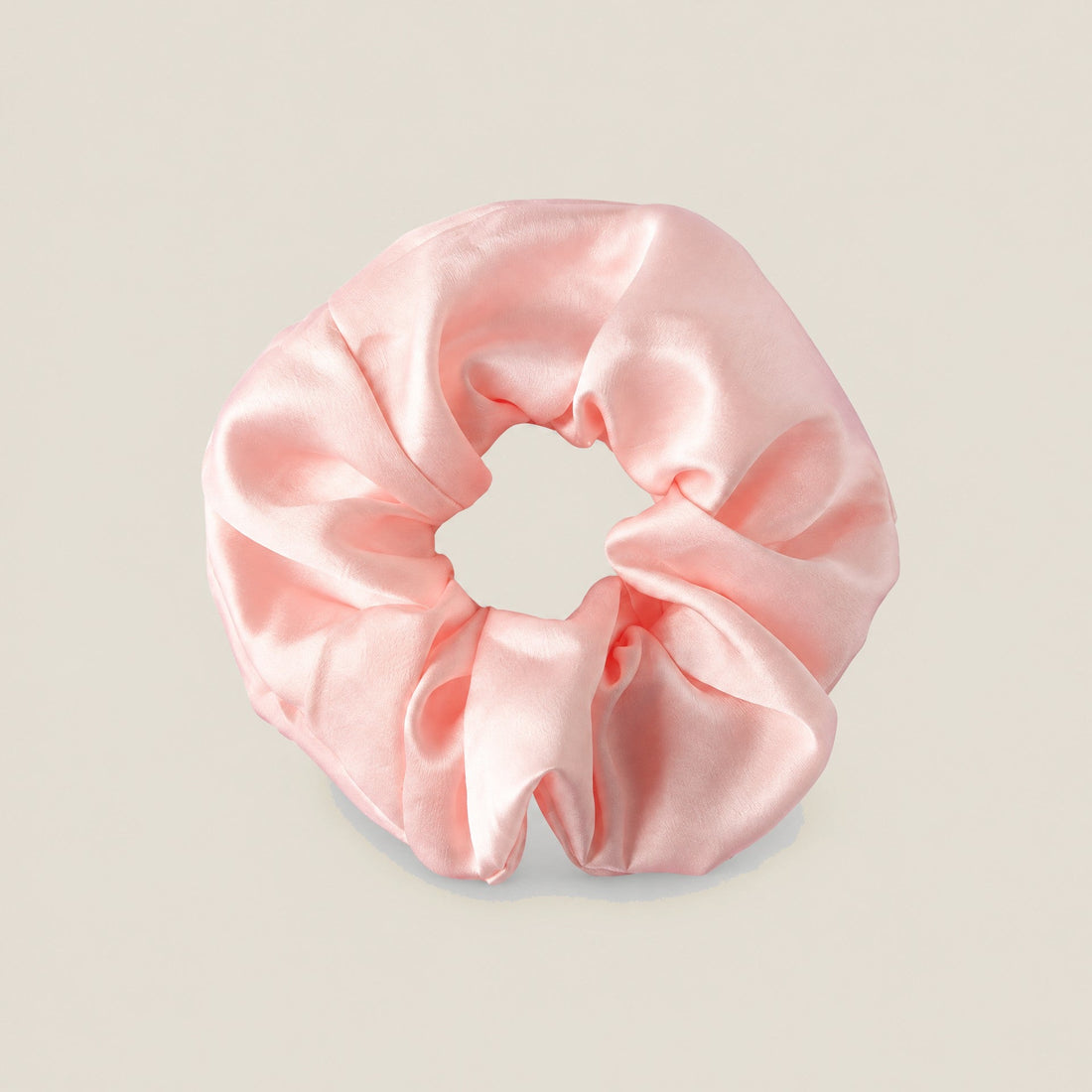 Close-up of a mint green satin scrunchie with a ruched, gathered design on a plain light beige background.
