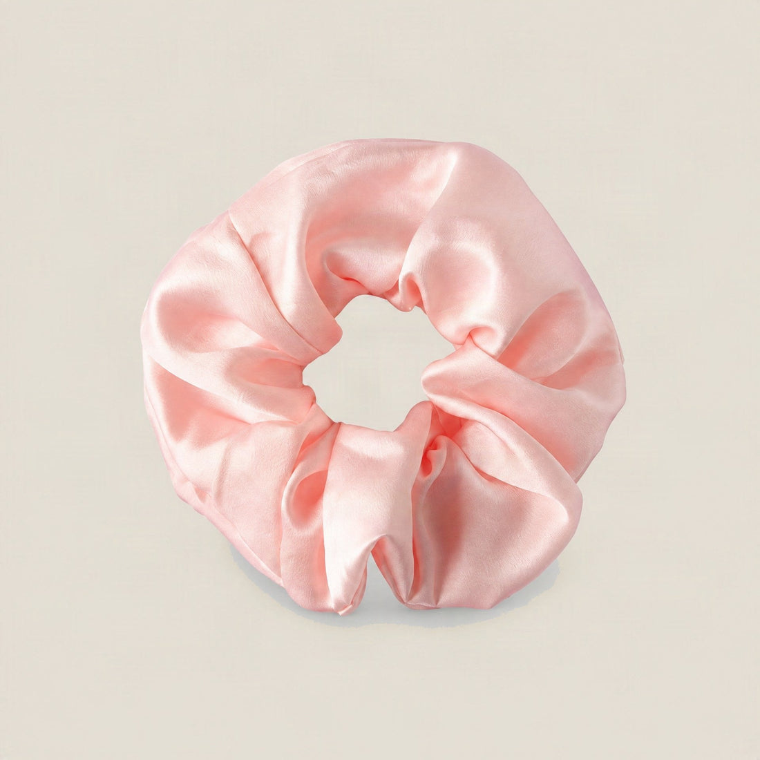 A mint green silk scrunchie with a ruched, gathered design resting on a light beige background
