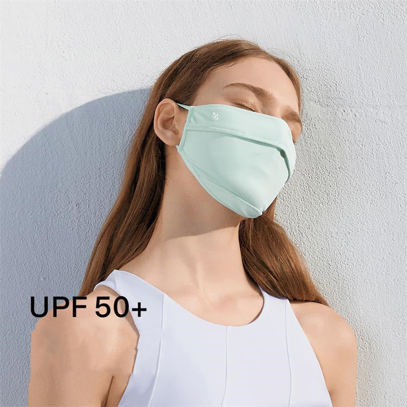 Woman with long brown hair wearing a light mint-green SUUMEE UPF50+ face mask against a white textured wall.