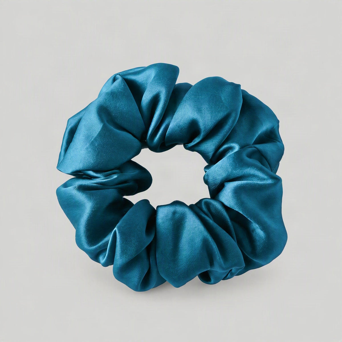 Mulberry silk scrunchie with soft ruffled edges in champagne color resting on a white marble surface