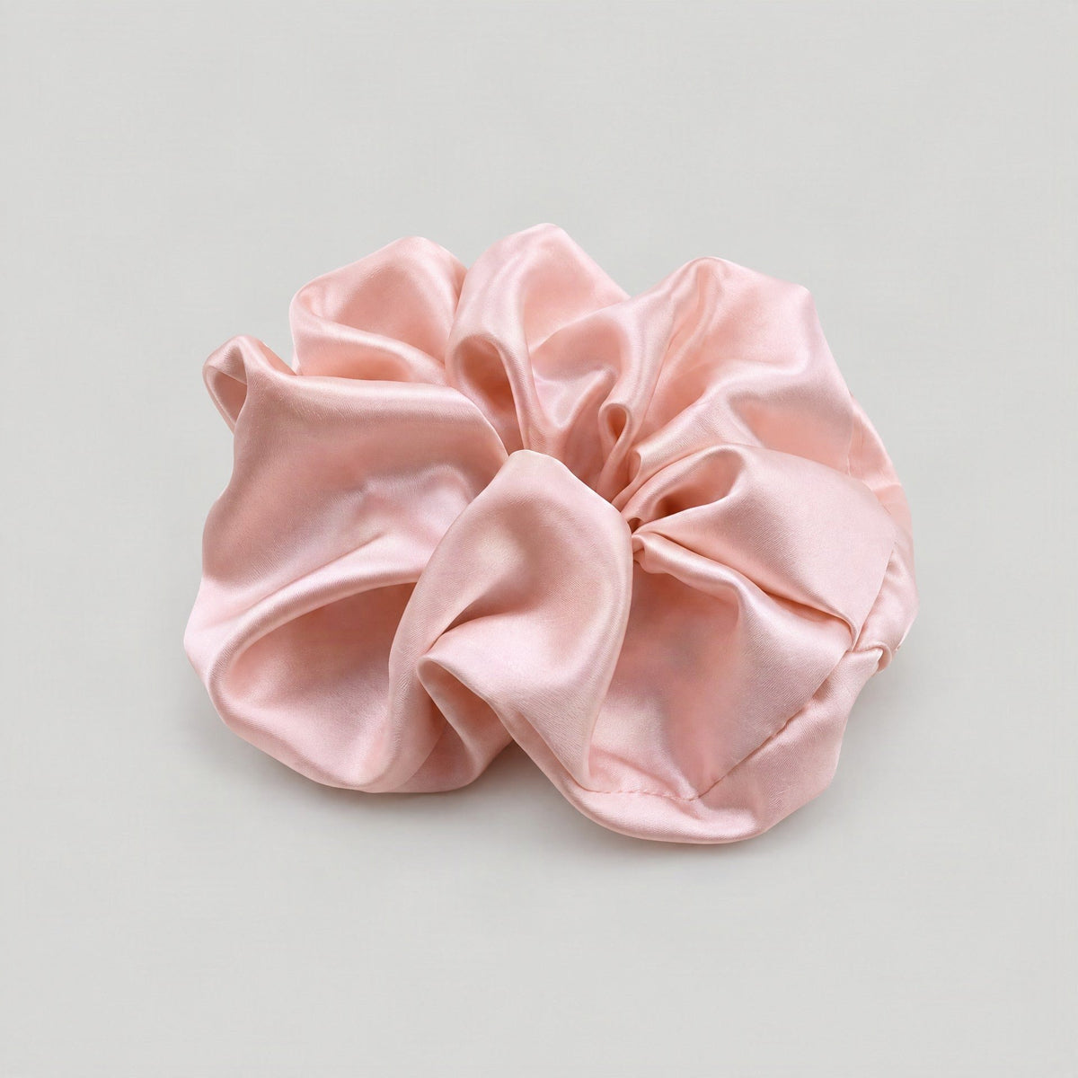 Lustrous champagne-colored 30 Momme mulberry silk scrunchie resting on a marble surface, showcasing its smooth sheen and gent