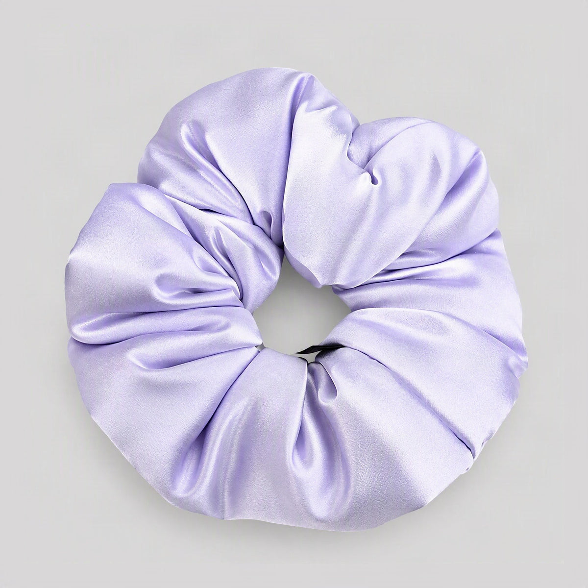 Padded mulberry silk scrunchie in 30 momme weave, resting on a soft beige surface for a gentle everyday hair accessory.