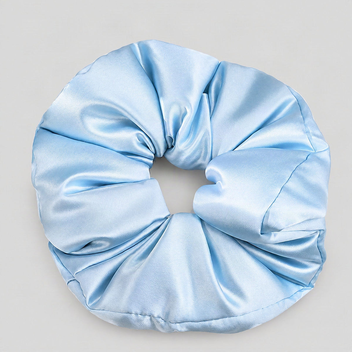 Soft champagne-colored 30 Momme Mulberry Silk scrunchie styled on a light surface beside a silk pillow, showcasing gentle hai