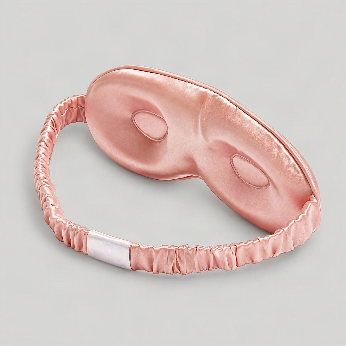 SuuSilk 19 Momme 3D Contoured Mulberry Silk Sleep Eye Mask in soft blush pink, resting on a bedside table.