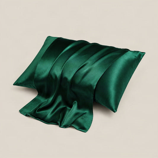 16 Momme silk pillowcase in coral draped on a bed with soft natural lighting, showing smooth double-sided envelope design.