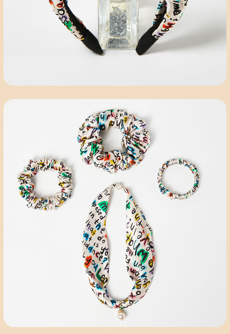 Flat-lay view of the letter print silk headband styled alongside matching scrunchies and accessories