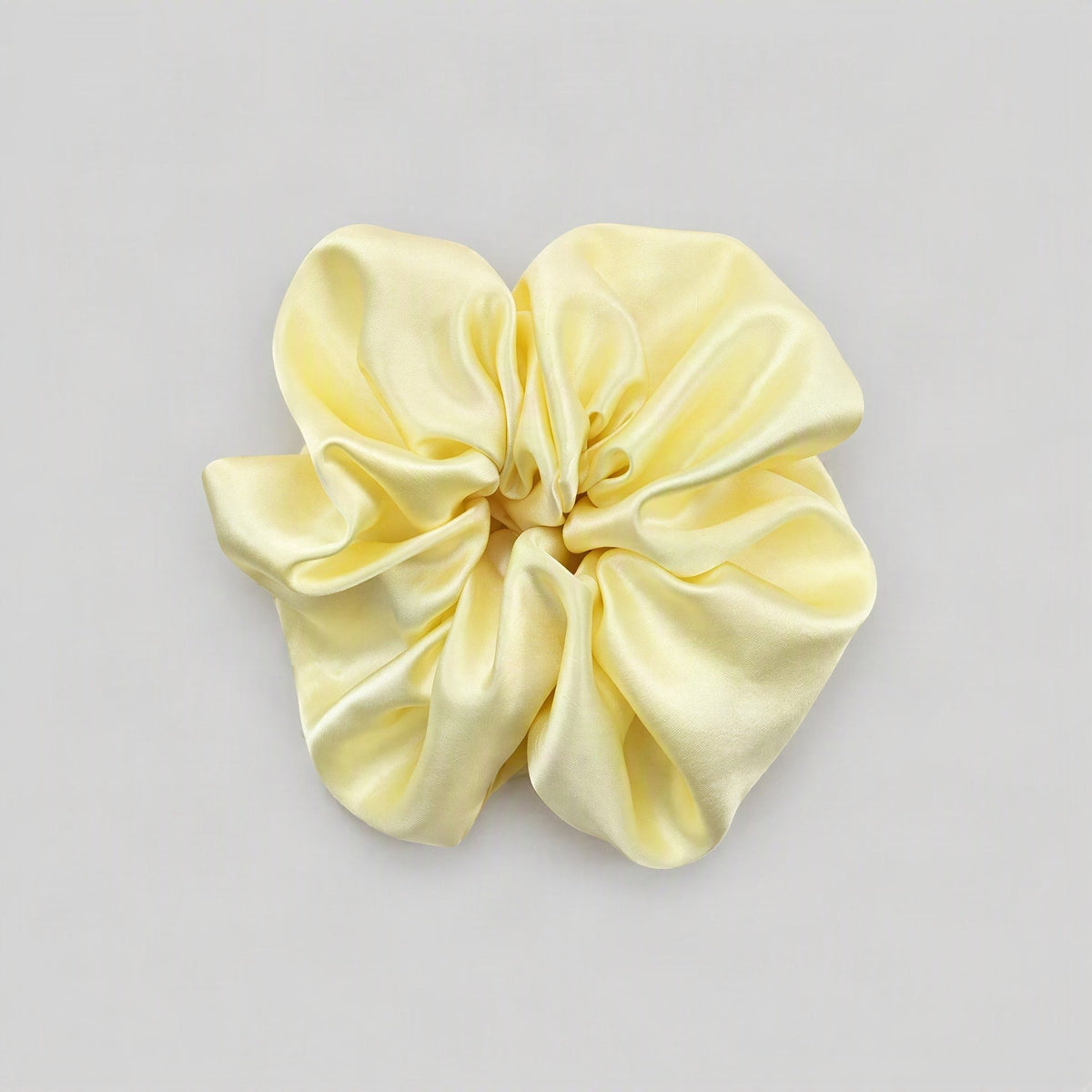 SuuSilk 30 Momme mulberry silk scrunchie in soft blush pink, draped on a marble surface with delicate floral accents