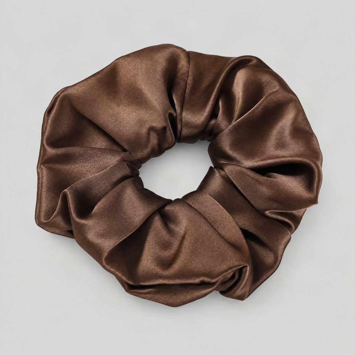 Mulberry silk scrunchie in soft blush pink resting on a neutral linen surface, showcasing its gentle sheen and smooth texture