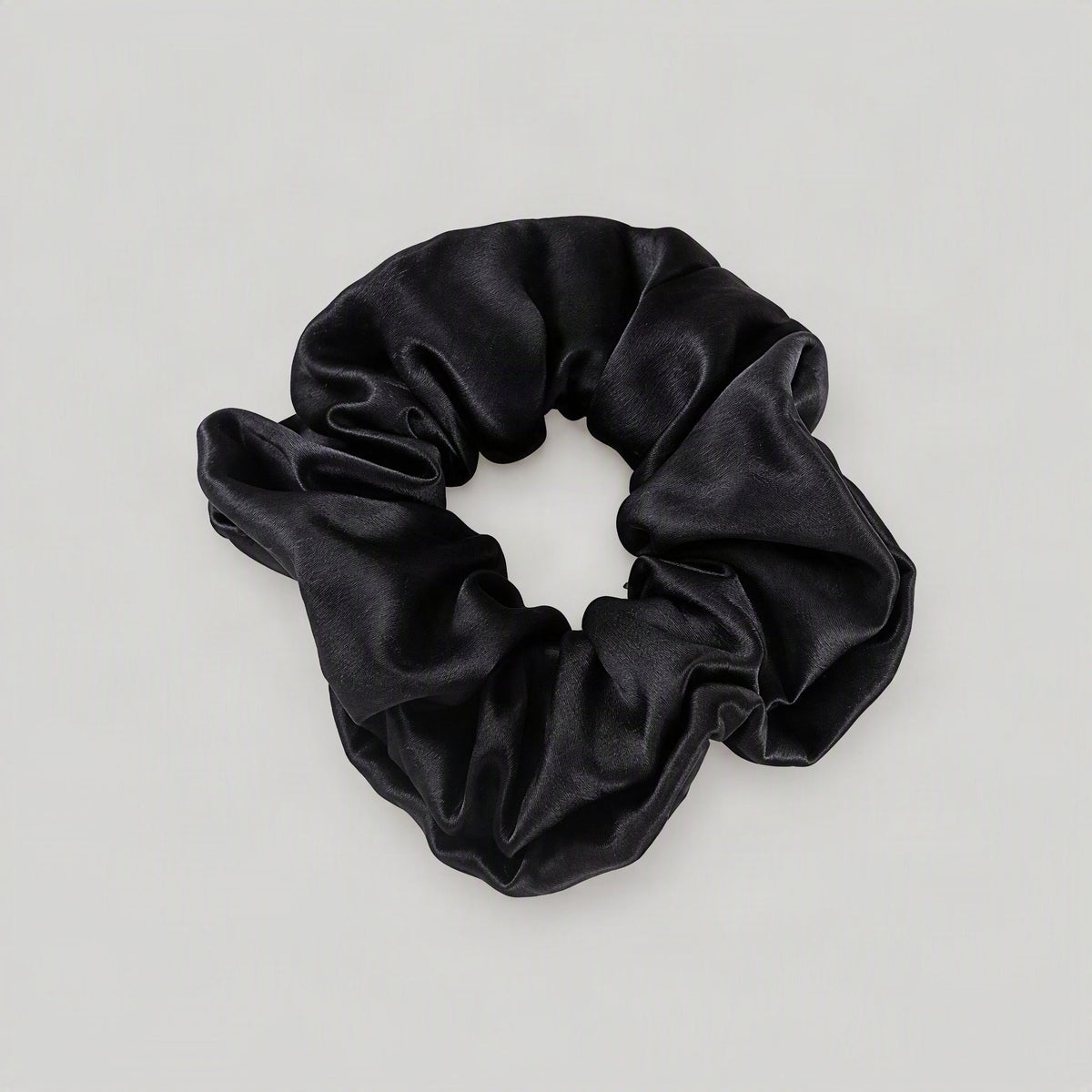 SuuSilk 30 Momme mulberry silk scrunchie in soft blush pink, draped elegantly on a marble surface highlighting its smooth she
