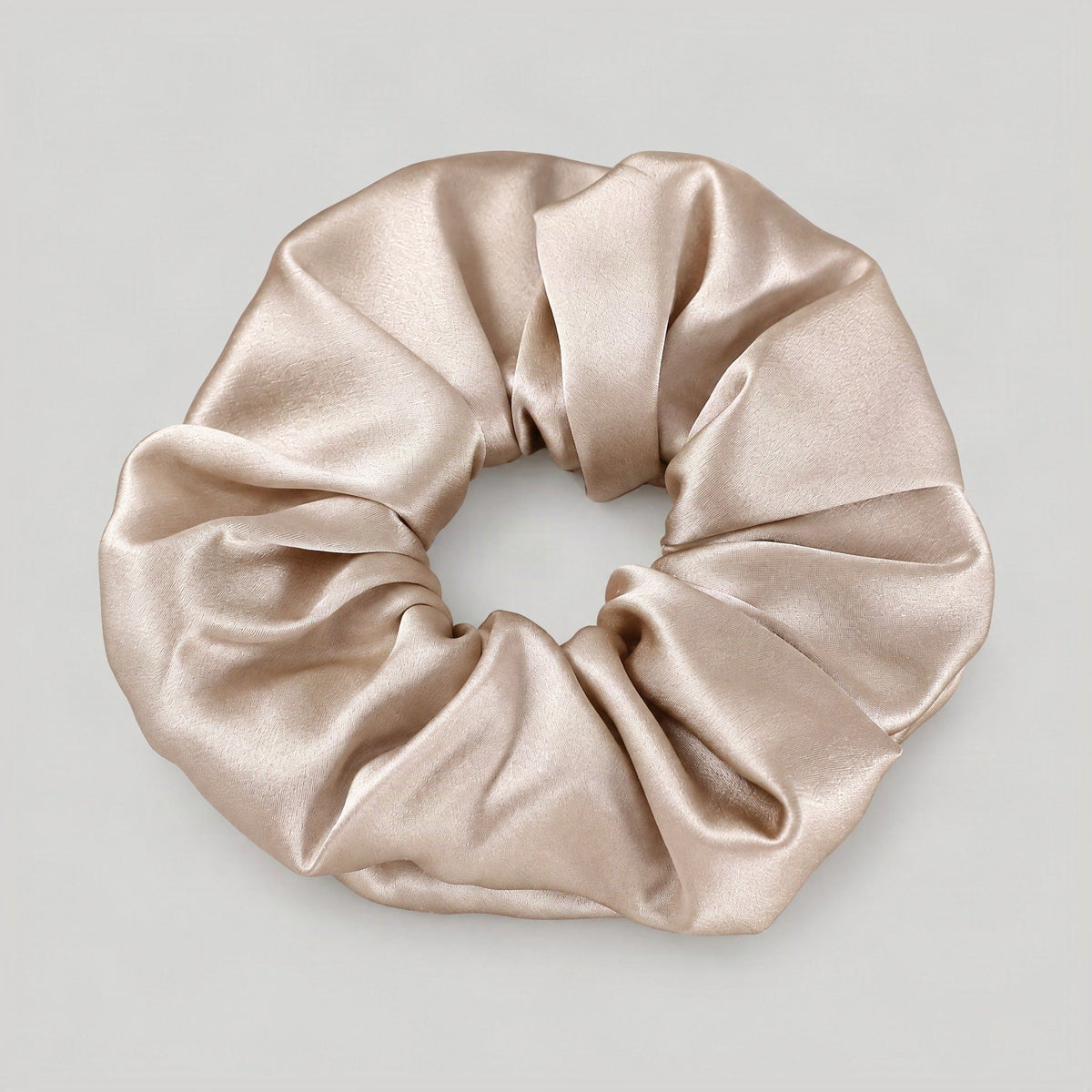 SuuSilk 30 Momme mulberry silk scrunchie in champagne, displaying lustrous sheen and soft folds on a marble vanity