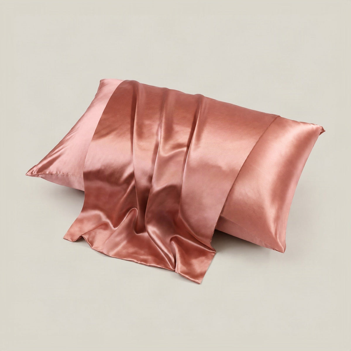 Silk envelope pillowcase in soft champagne laid on a linen bed beside a coffee cup and book, glossy mulberry texture visible.