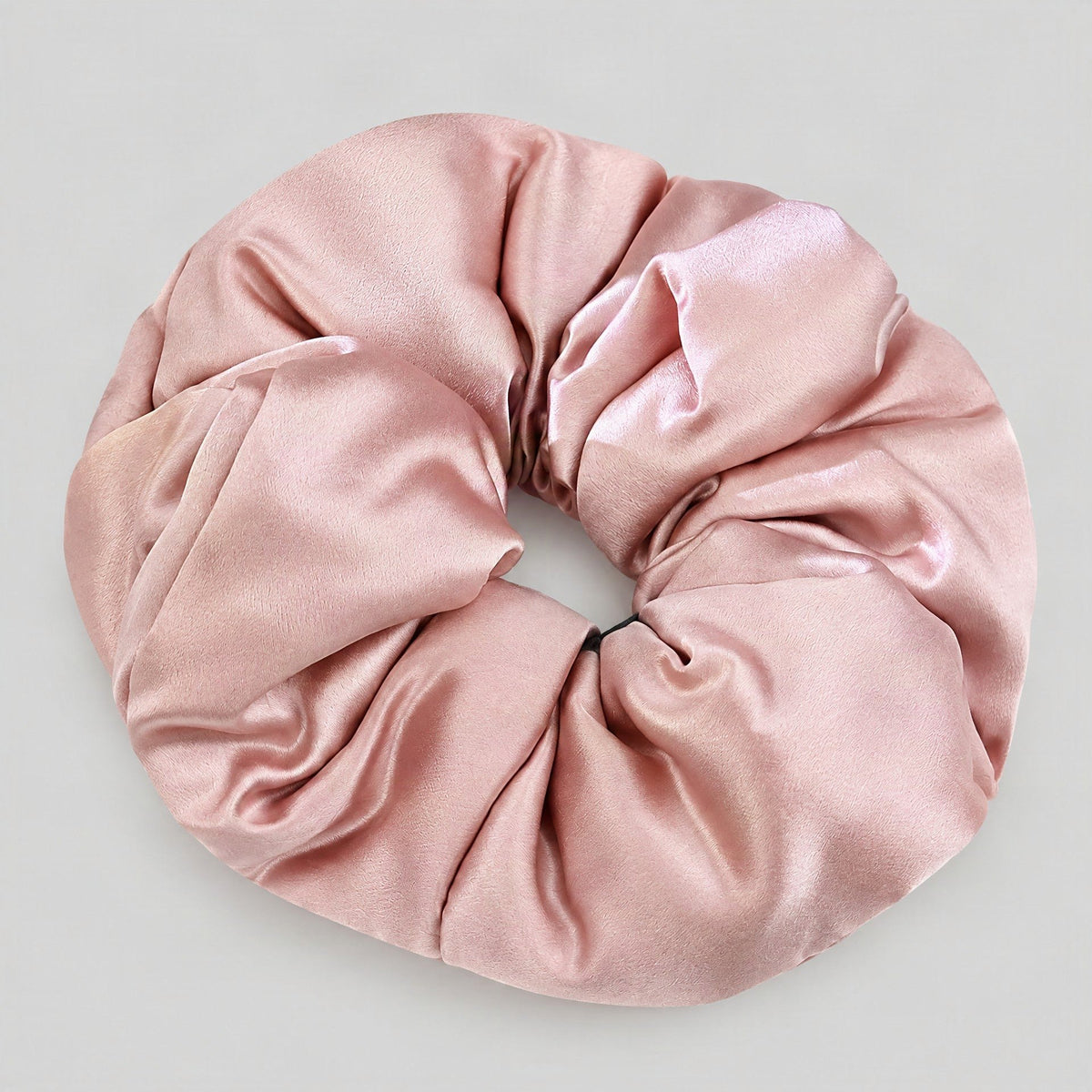 Silk scrunchie in soft beige resting on a white marble surface, gentle everyday hair accessory